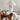 Cat looking at an open book on a wooden table with a lamp and decorative items.