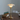 Table lamp with a gold base and white shade on a wooden table with books in the background.