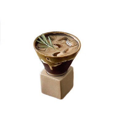 A handcrafted ceramic cup with a brownish-tan finish, displayed on a beige stand, with a green plant inside.