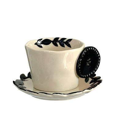 A beige ceramic button cup with black leaf patterns on the cup and saucer.