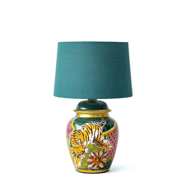 A table lamp with a green linen lampshade and a ceramic base featuring a colorful floral and animal pattern.