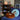Two plush donut-shaped floor cushions in brown and light blue, styled on a blue sofa in a cozy living room setting with a bookshelf and posters in the background.