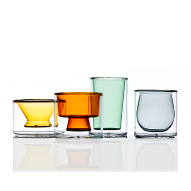 A selection of borosilicate glass glassware in varying colors, including clear, green, amber, and white, arranged in a row.