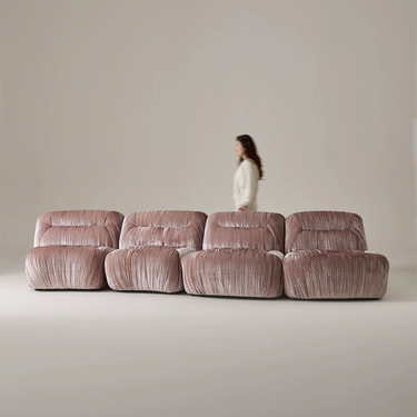 Large pink sofa with a person standing behind it against a plain wall.