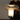 A person holding a modern mushroom-shaped table lamp with a clear glass shade and a glowing white illuminated base on a silver metal base, set against a plain gray wall.