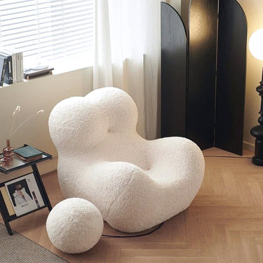 White fluffy chair and ottoman in a room with a window and side table.