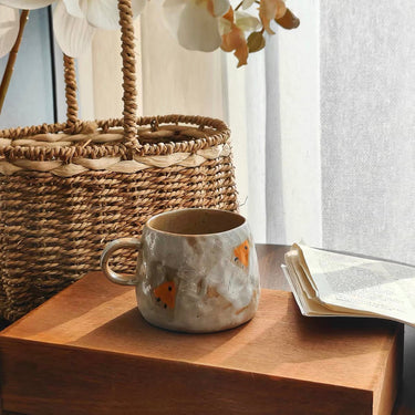 Ceramic mug with fish design on a wooden surface next to a woven basket and open book.
