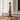 A tall, abstract wooden sculpture with stacked organic shapes on a rectangular base, displayed in a minimalist interior setting with books and a white vase on a shelf.